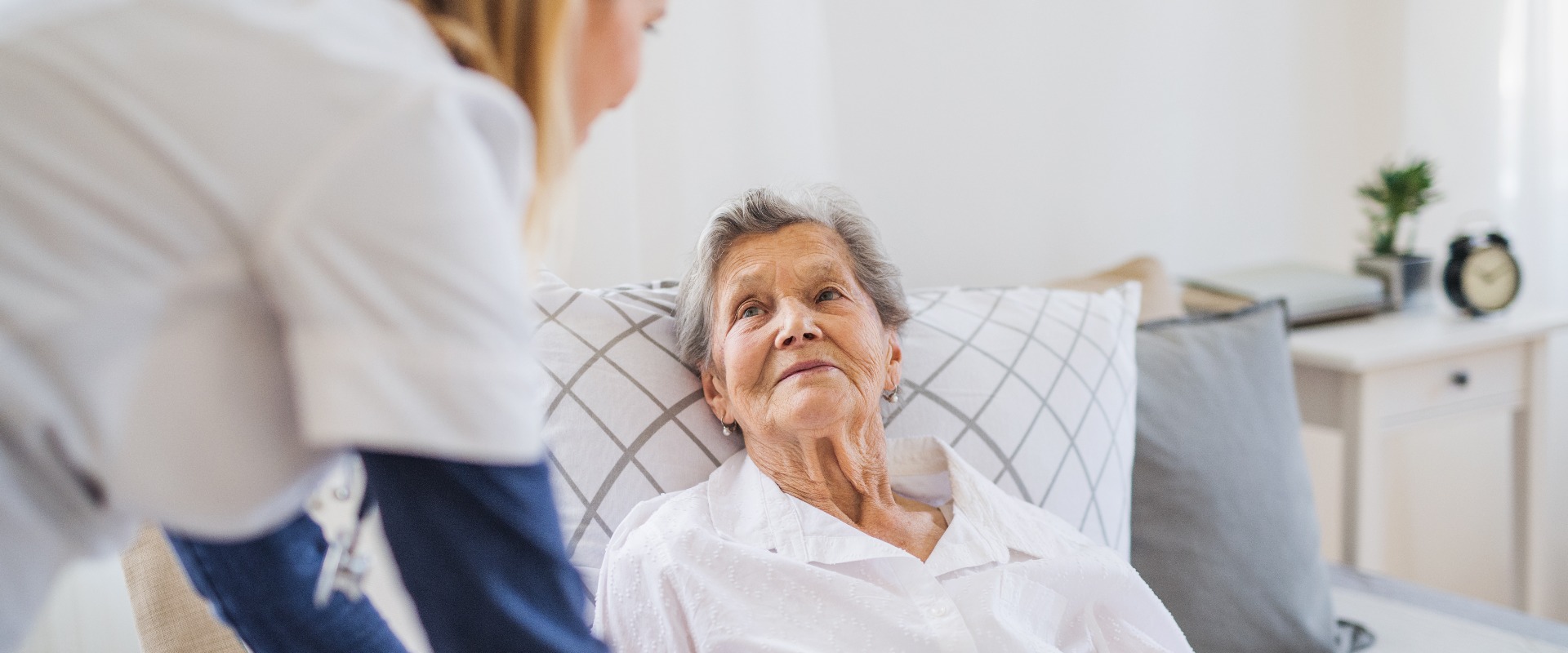Eine Gesundheitsberaterin im Gespräch mit einer kranken älteren Frau, die zu Hause im Bett liegt.