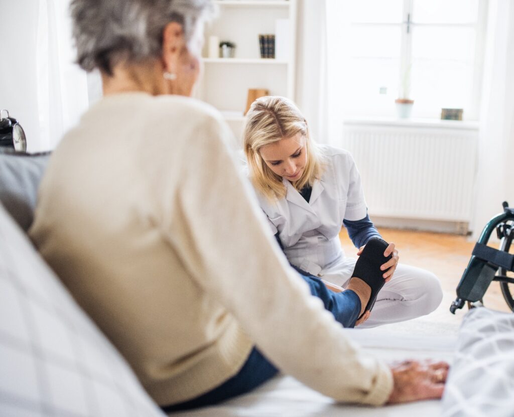 Eine Gesundheitsberaterin zieht einer älteren Frau zu Hause Hausschuhe an.
