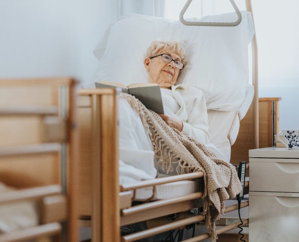 Eine kranke ältere Frau liegt in einem Krankenhausbett und liest ein Buch